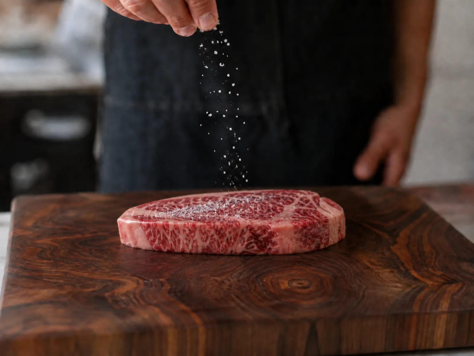 A Kangen Wagyu ribeye being seasoned on a walnut board